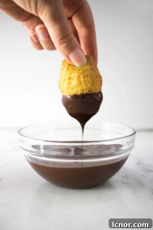 hand dipping a madeleine into a bowl of chocolate