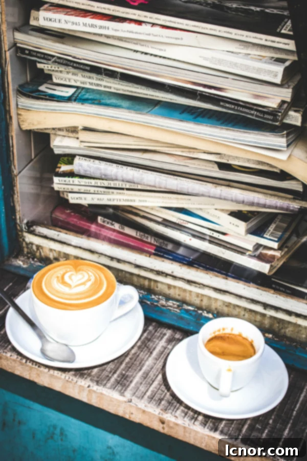 Two coffee cups, an espresso and a flat white, on a table in a stylish Parisian cafe, with Vogue magazines in the background.
