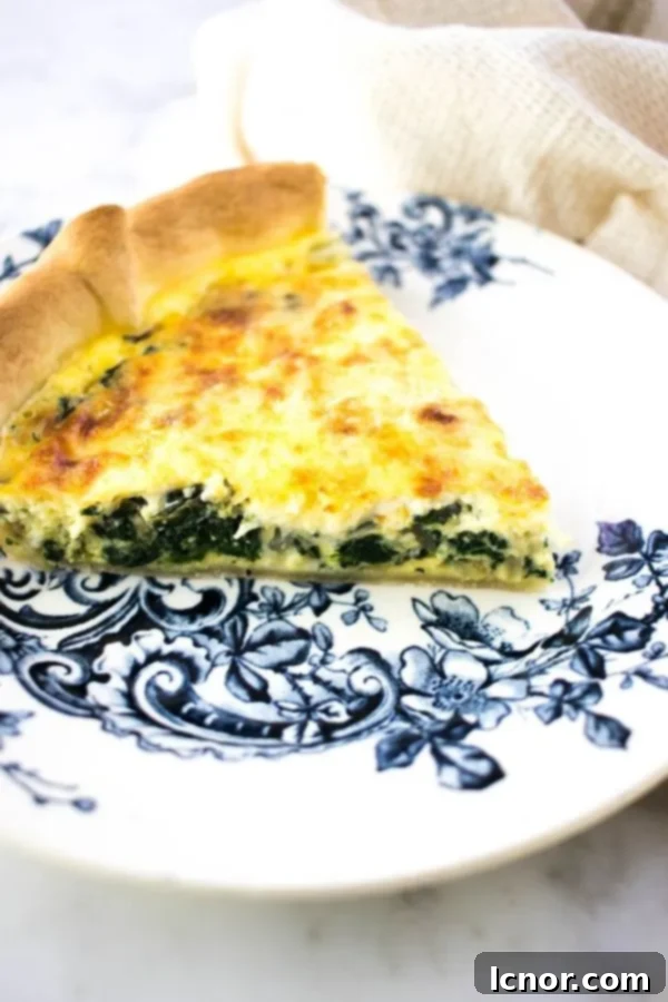 a slice of yellow cheese and spinach Florentine quiche seen from the side on a blue and white floral plate