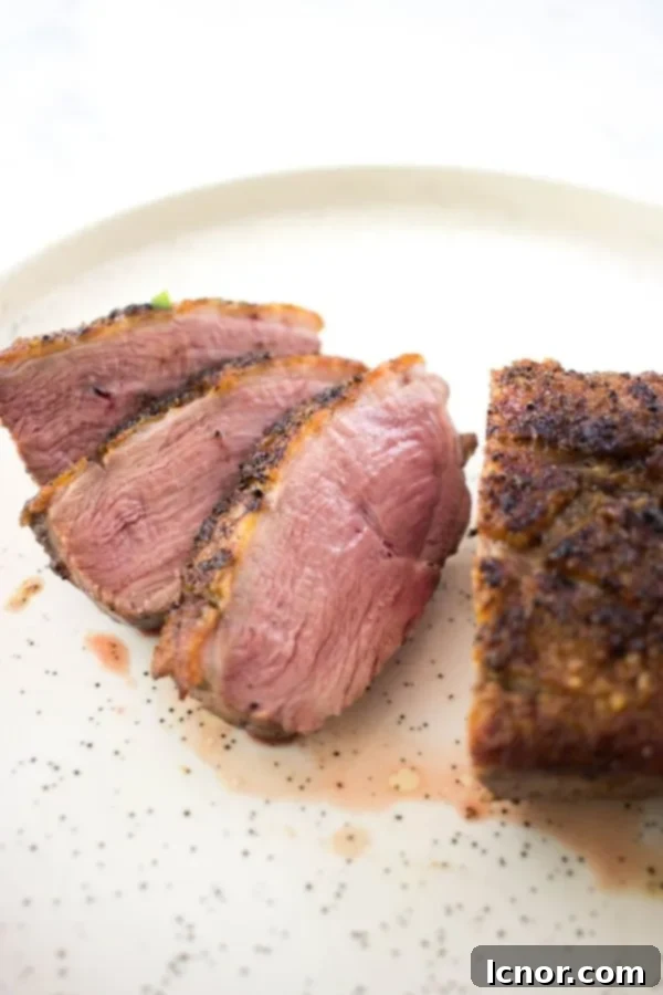 Perfectly sliced Magret de Canard showcasing its rosé interior, served on a white speckled plate.