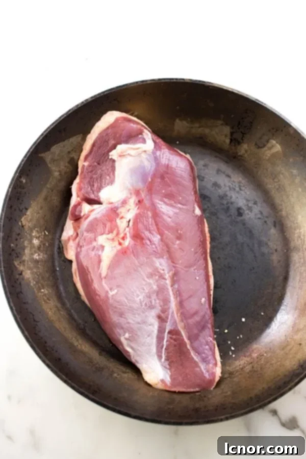 Raw duck breast, skin-side down, placed in a black frying pan, ready to be cooked.