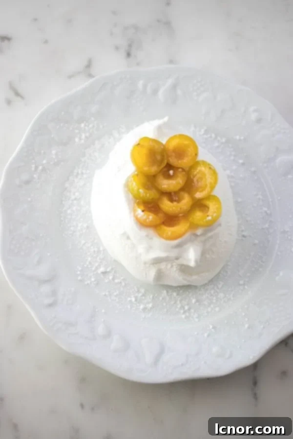 Close-up of a perfectly baked Schaum Torte tartelette topped with golden yellow mirabelle prunes and fluffy whipped cream, showcasing its elegant presentation.
