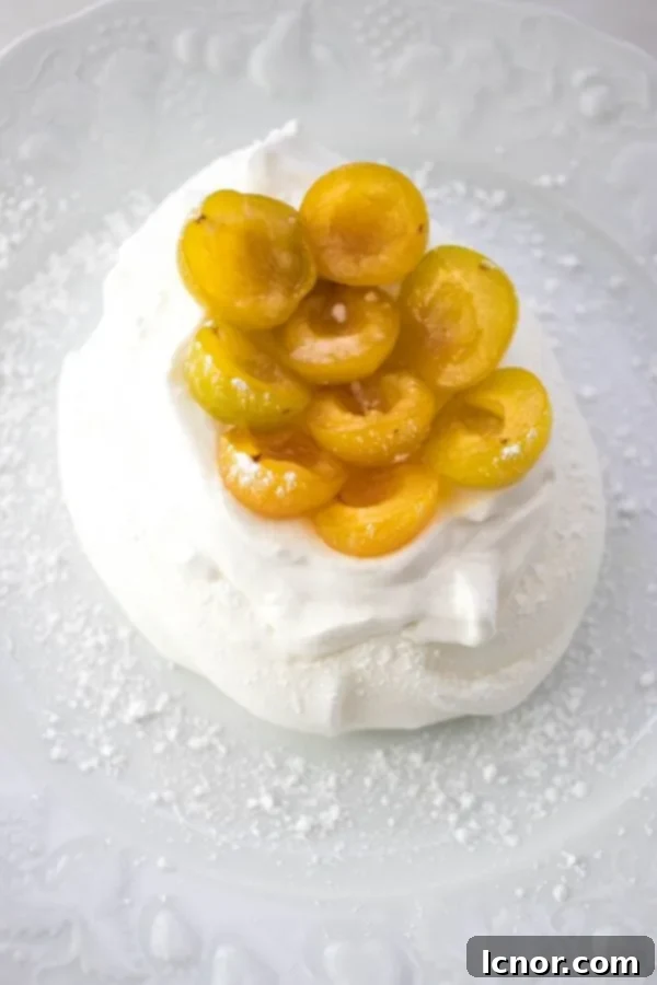 Two exquisite mini Schaum Torte desserts, each featuring a golden meringue nest filled with whipped cream and topped with fresh yellow mirabelle prunes, on a white background.