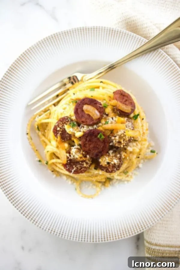 A close-up of spaghetti with chorizo in a white and gold bowl, featuring a gold fork, highlighting the vibrant ingredients.