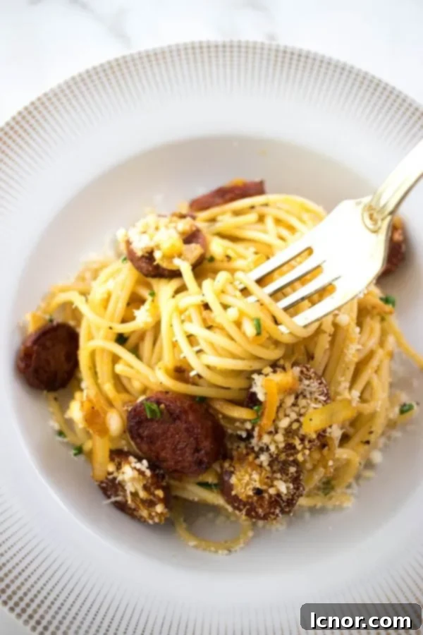 A gold fork twirling into a generous portion of creamy chorizo pasta, showcasing the rich, red hue of the sauce and the fresh green chives.