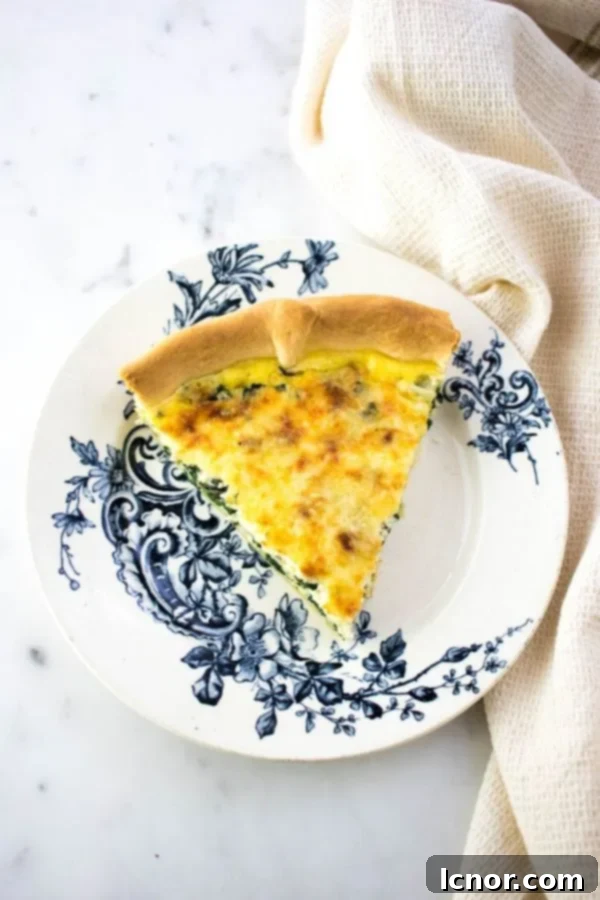 A beautiful slice of French spinach quiche (Quiche Florentine) on a white and blue patterned plate.