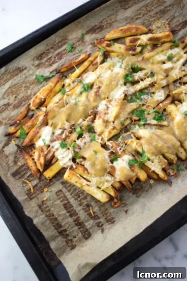 Delicious oven baked Disco Fries, generously topped with savory gravy, melted mozzarella cheese, and fresh parsley, served on a baking sheet.