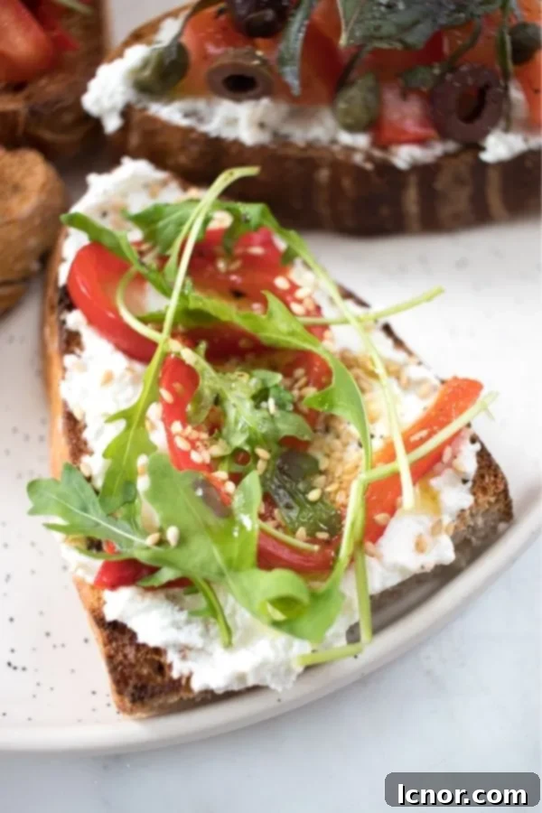 A vibrant bruschetta slice topped with creamy ricotta cheese, strips of roasted red peppers, and fresh green arugula or rocket salad, all on toasted bread.