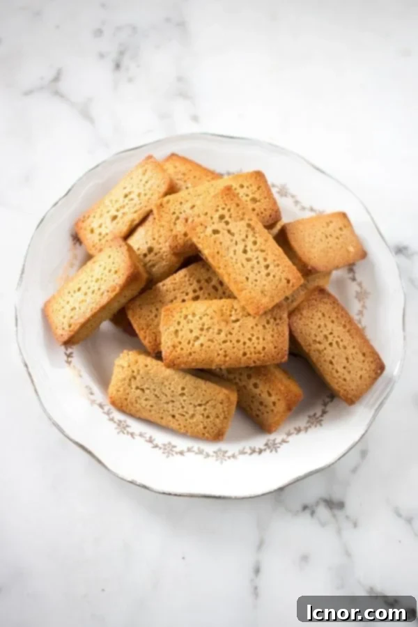 French brown butter financiers stacked on a vintage French plate, highlighting their golden-brown crust and elegant shape.