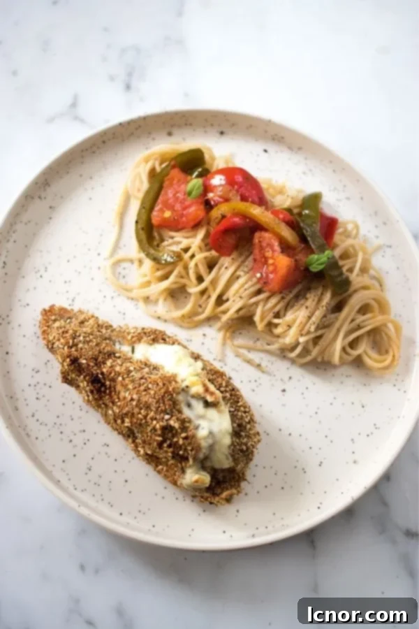 Philadelphia stuffed chicken topped with sesame seeds and spaghetti topped with tomatoes and peppers on a white and black speckled plate, a perfectly plated meal