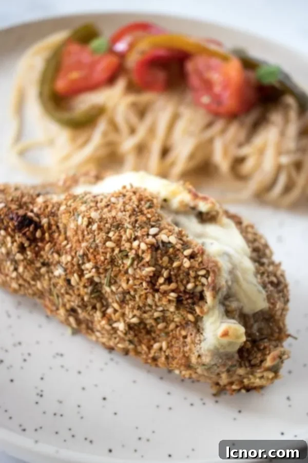 Philadelphia chicken close-up topped with sesame seeds on a white and black speckled plate with spaghetti in the background