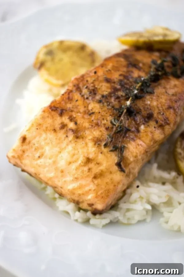 salmon meunière on a white plate with white rice and lemon slices on the side