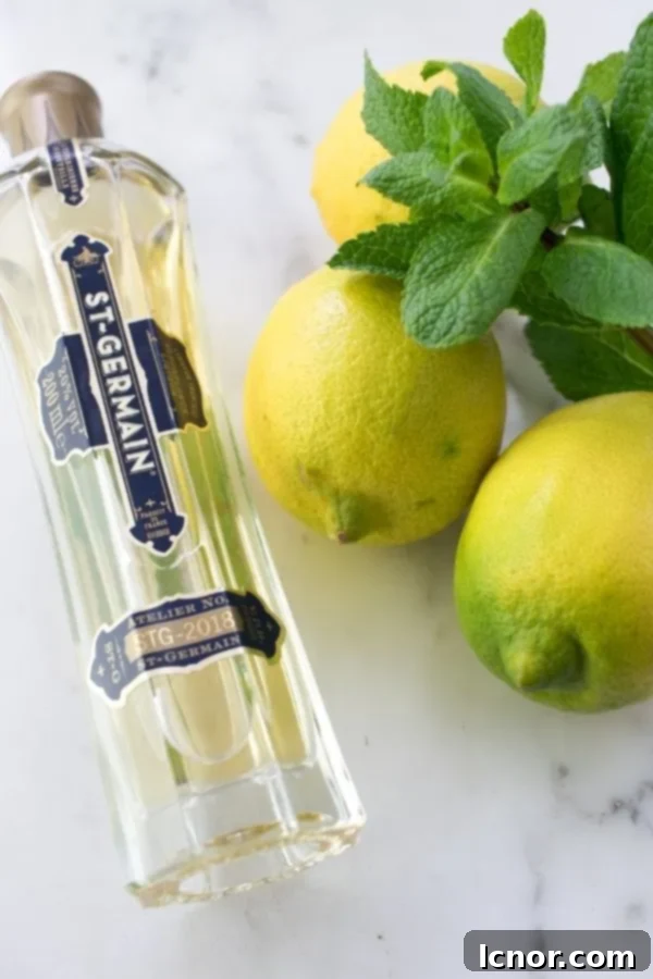 A bottle of St. Germain elderflower liqueur, fresh lemons, and vibrant mint leaves, essential ingredients for a Hugo Spritz