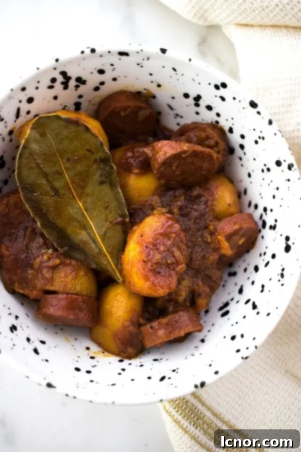 Spanish chorizo con patatas in a white and black bowl topped with a bay leaf, ready to serve