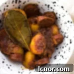 Spanish chorizo con patatas in a white and black bowl topped with a bay leaf