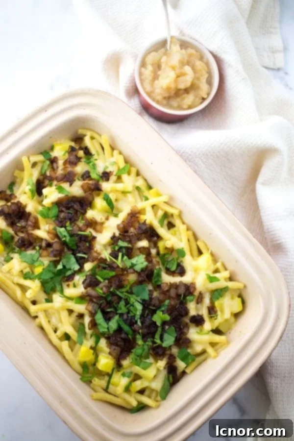 A baking dish filled with golden-brown Älplermagronen (Swiss Alpine Macaroni), garnished with fresh parsley and a side of smooth applesauce.