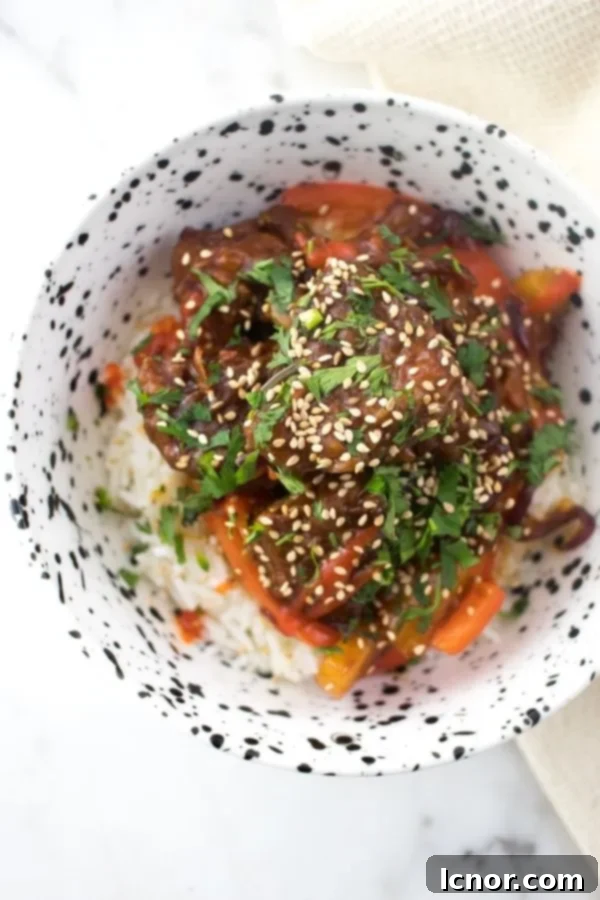 Sweet and Sour Pork Kou Lou Yuk on white rice in a bowl, garnished with sesame seeds and cilantro, ready to be served.