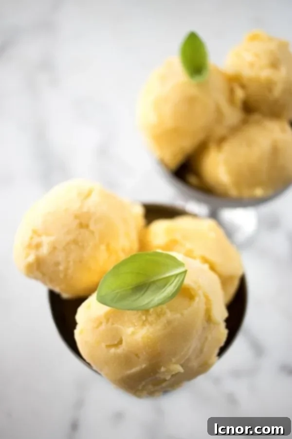 Filipino Mango Ice Cream on a white and grey marble table, garnished with fresh mint.