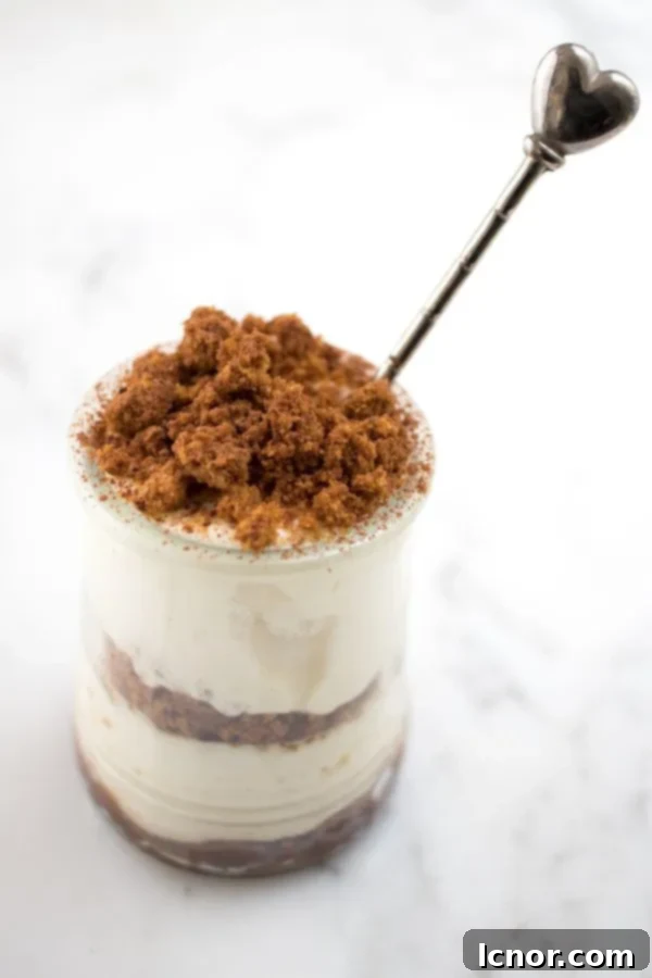 Biscoff tiramisu in individual jars, garnished with crushed biscuits and a heart-shaped spoon.