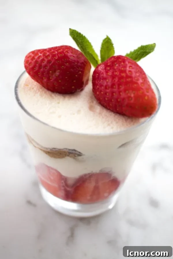 a cup with tiramisu all fragile inside with two strawberries on top, served in a glass