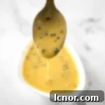 a golden spoon dripping a bright yellow mustard sauce