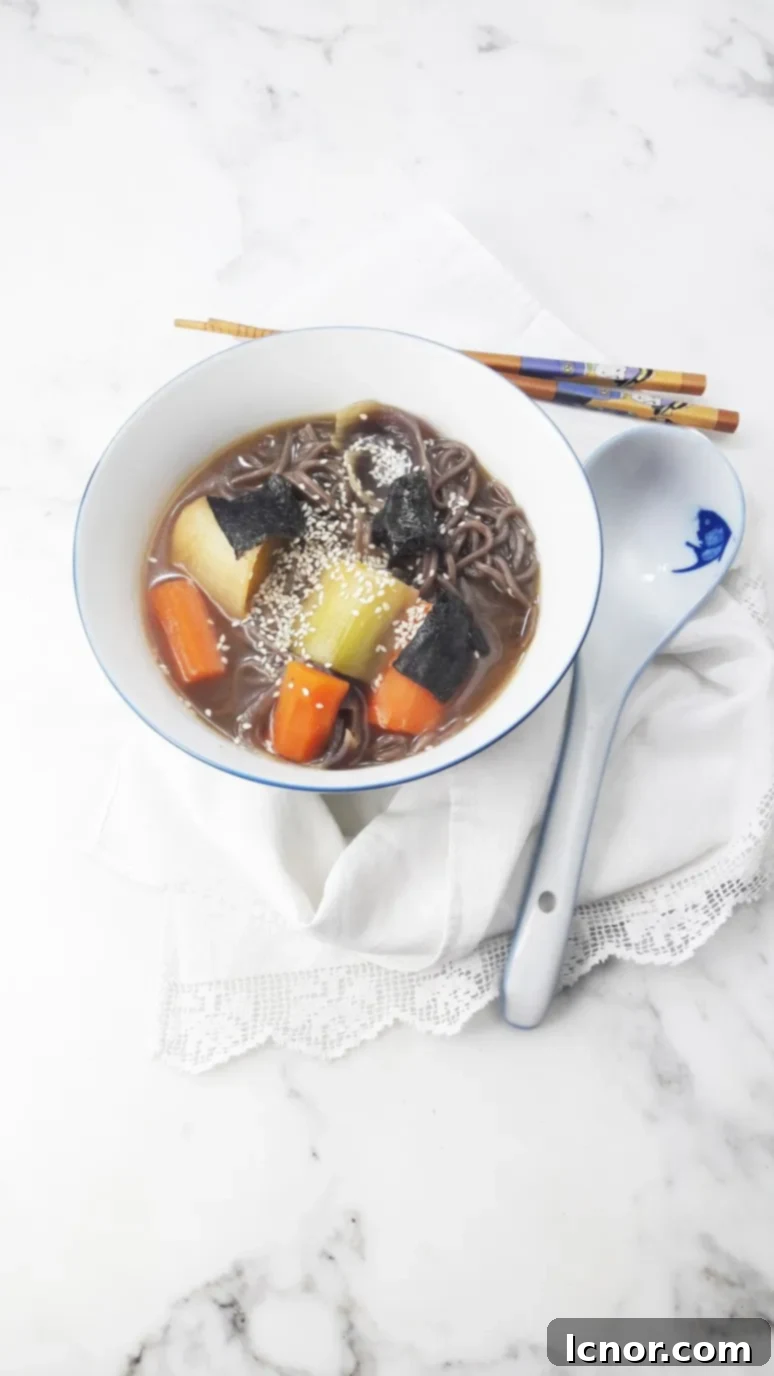 Stylishly presented bowl of miso soup with visible leeks, carrots, noodles, and seaweed garnish.