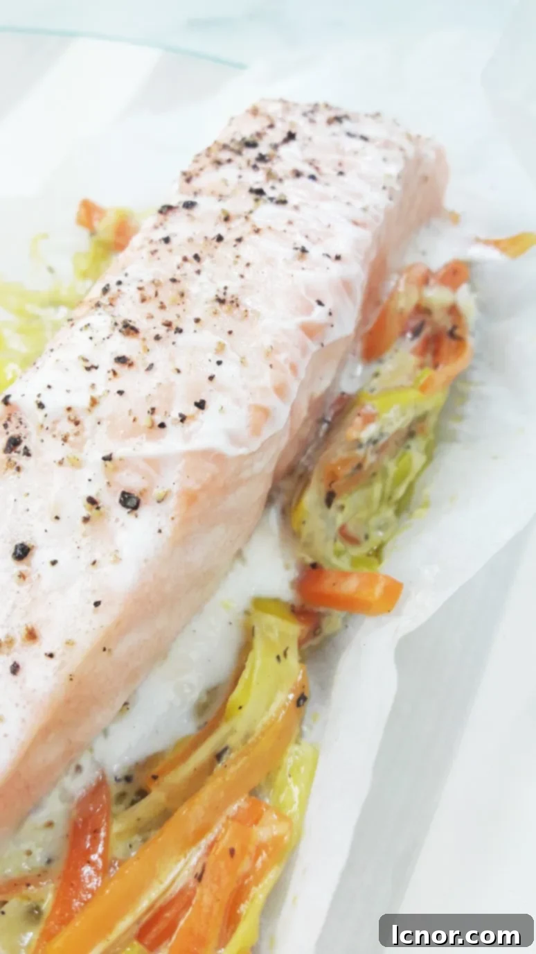 The salmon, leeks, and carrots baked in parchment paper are ready to be served, steaming gently as the packet is opened.