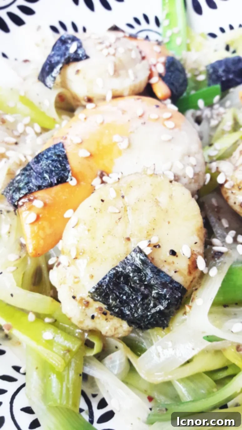 Close-up of succulent Japanese miso scallops arranged over a bed of tender leek noodles, garnished with sesame seeds and nori strips. A gourmet seafood dinner ready in minutes.