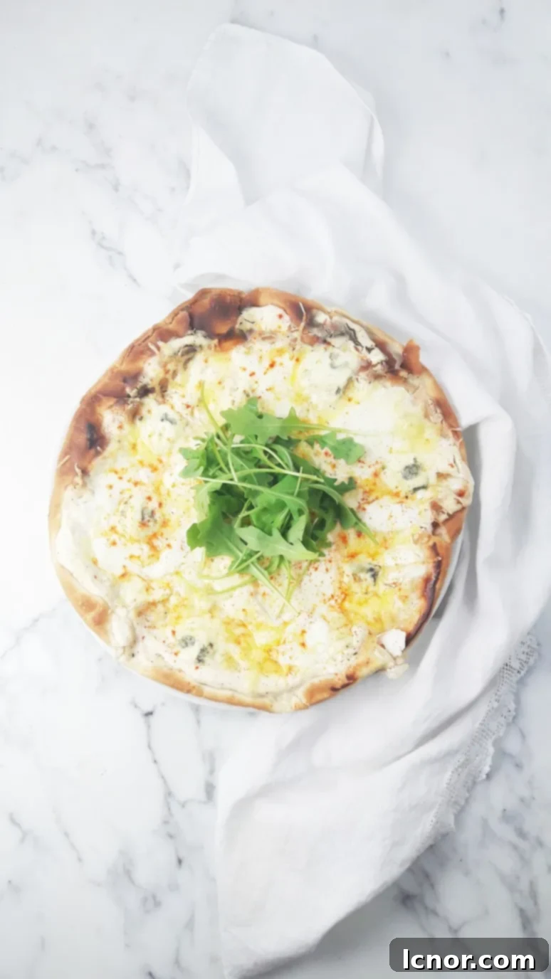 Close-up of a perfect white 4 cheese pizza dripping with melted blue cheese, Emmental, Buffalo mozzarella, & ricotta, generously topped with fresh rocket salad and spicy red pepper flakes, served on a rustic wooden board. | ahedgehoginthekitchen.com