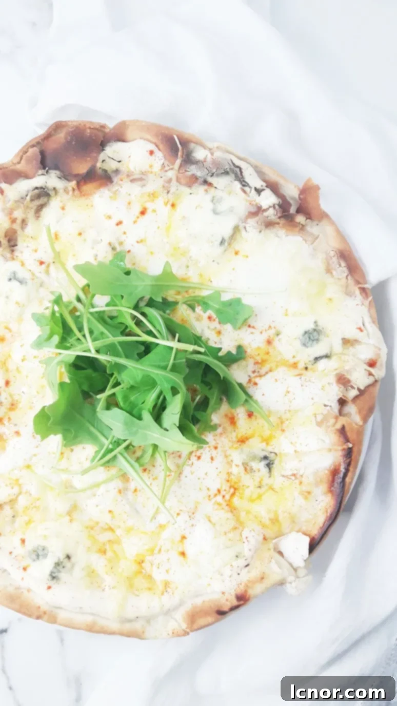 A slice of perfect white 4 cheese pizza being pulled from the main pie, showcasing the melted cheese stretch and the fresh rocket topping. | ahedgehoginthekitchen.com