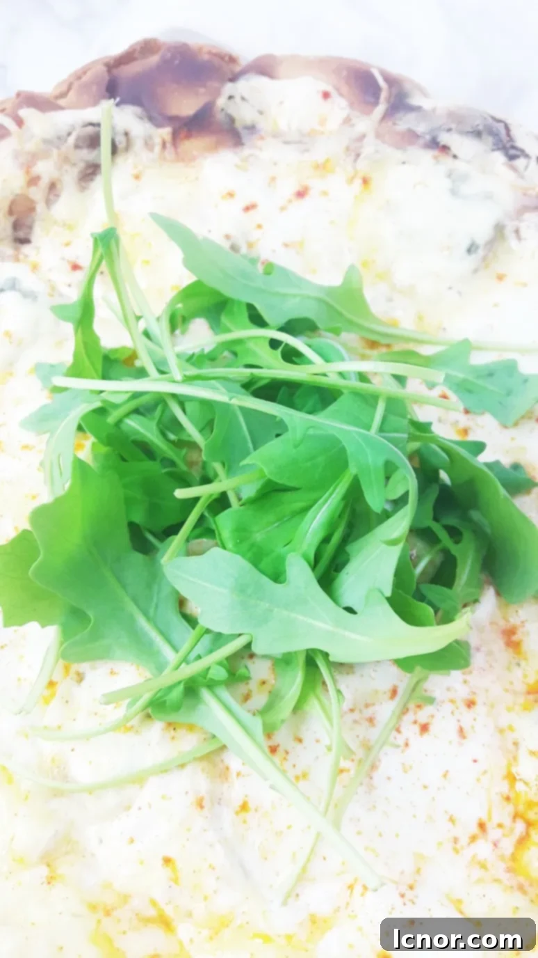Overhead view of a delectable white 4 cheese pizza, featuring melted blue cheese, Emmental, Buffalo mozzarella, & ricotta, elegantly topped with fresh rocket and a dash of spicy pepper. | ahedgehoginthekitchen.com