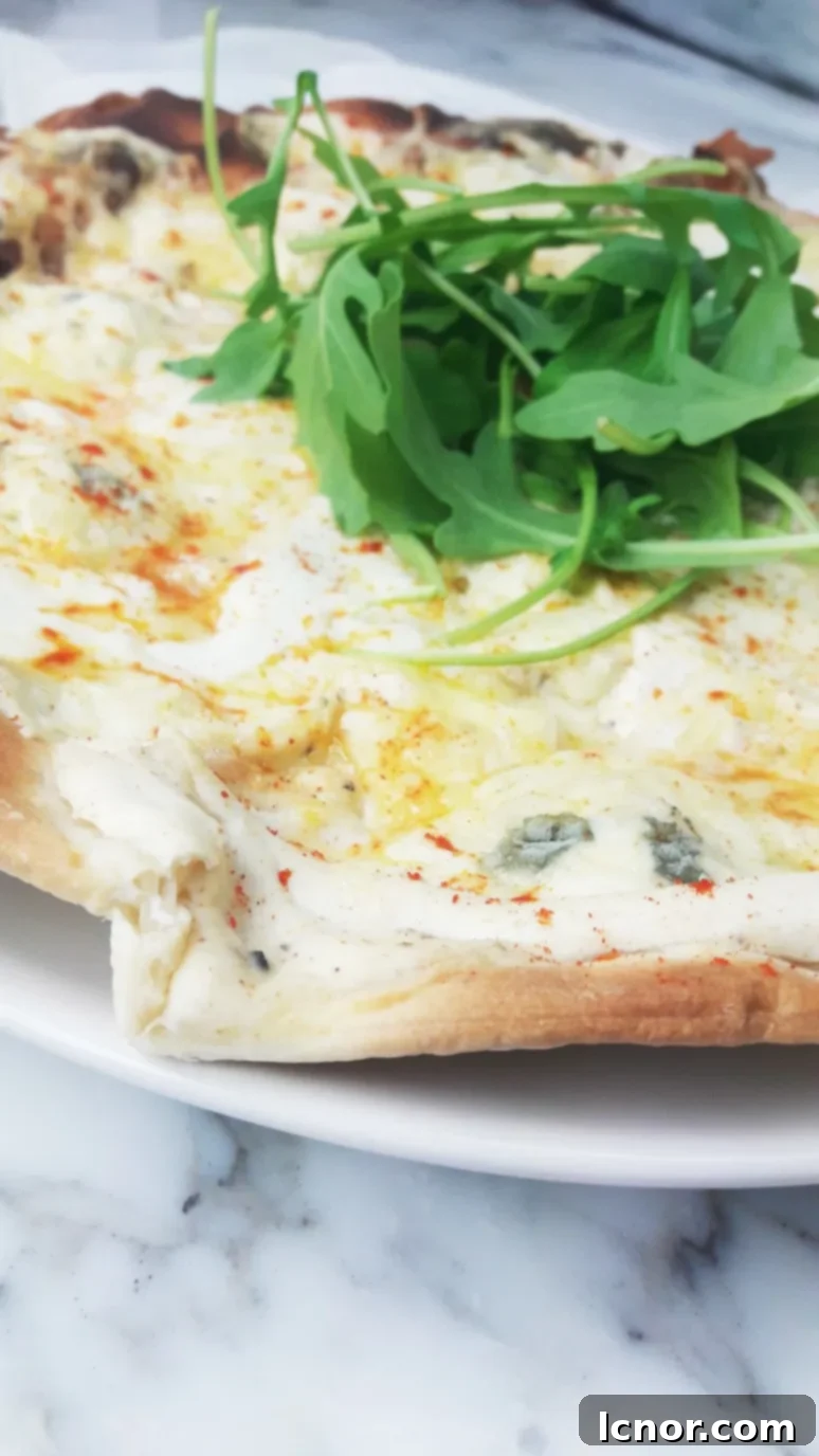 A whole perfect white 4 cheese pizza on a rustic wooden board, topped with abundant fresh rocket and spicy pepper, ready to be sliced and served. | ahedgehoginthekitchen.com