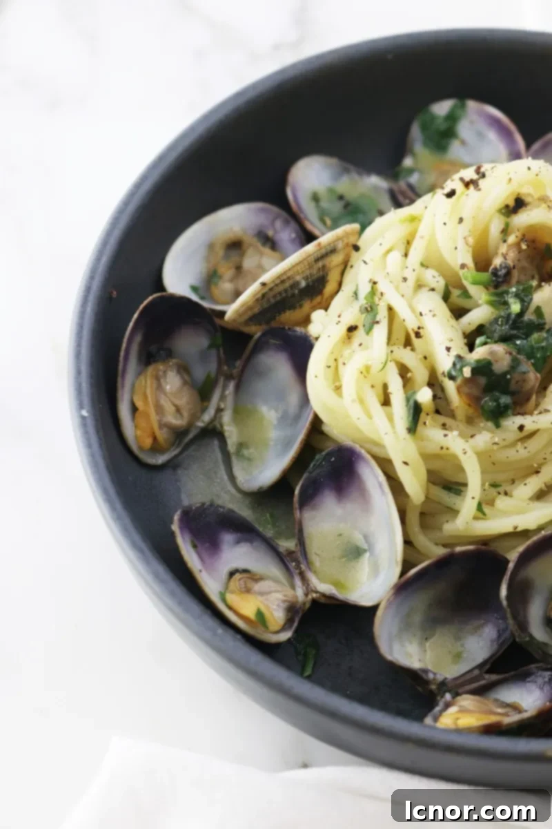 Assortment of fresh ingredients for Spaghetti alle Vongole, including raw clams, uncooked spaghetti, garlic, parsley, and white wine bottle.