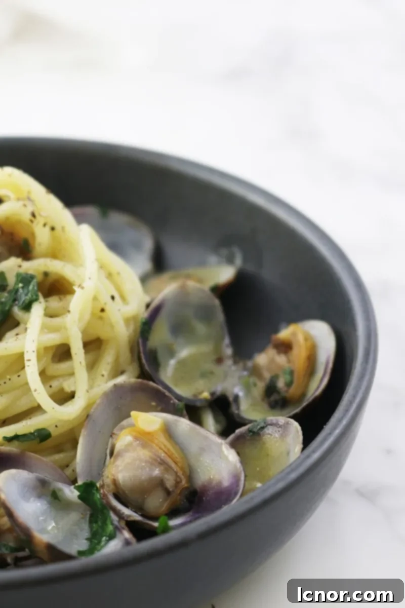 Spaghetti alle Vongole being expertly tossed in a large pan, mixing clams and sauce, creating a perfect emulsion.