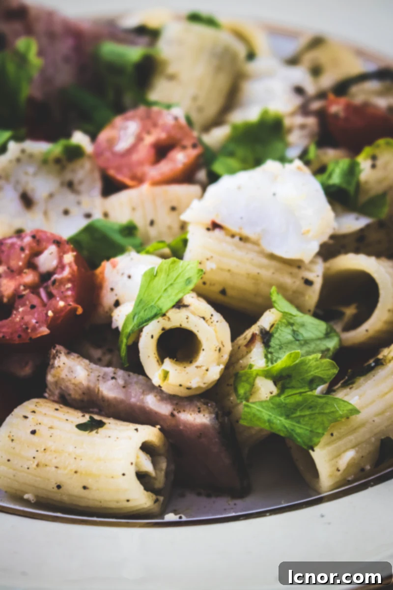 Gourmet fish pasta featuring cod, tuna pastrami, and vibrant cherry tomatoes, ready to serve