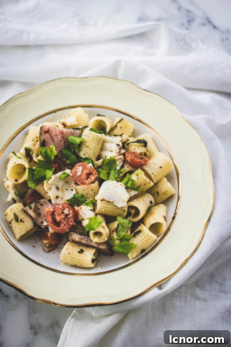 Artfully plated fish pasta with cod, tuna pastrami, and tomatoes, garnished with fresh herbs