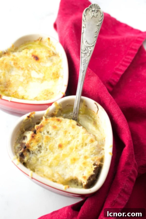 vegetarian French Onion Soup in French onion soup bowls topped with cheese with a silver spoon and red tea towel