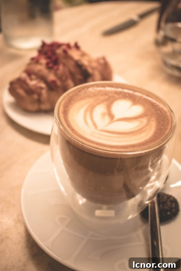 cappuccino with a heart on top and croissant in the background, signaling a perfect start to the day at 86 Champs