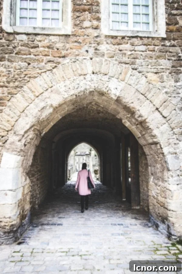 woman in a pink coat walking through a chateau arch in Northern France