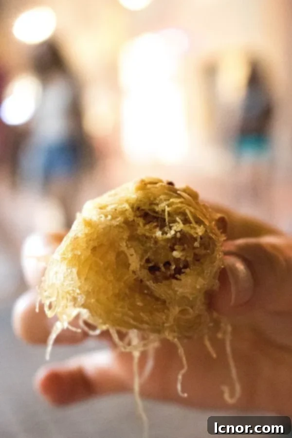 Kataifi - the best Greek dessert. A large piece being held up. This dessert needs to be on your Athens Food List.