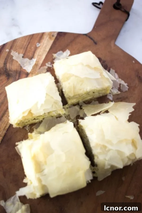 Tiropita (Greek Cheese Pie) cut into 4 small squares on a wooden cutting board, showcasing its golden, flaky layers and creamy filling.