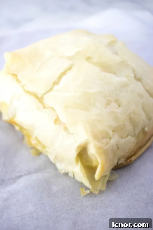 Tiropita (Greek Cheese Pie) - a large square on a cutting board and parchment paper, ready to be cut.