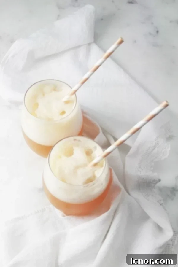 Two frozen apple cider cocktails in tall glasses, garnished with apple slices, on a white background.