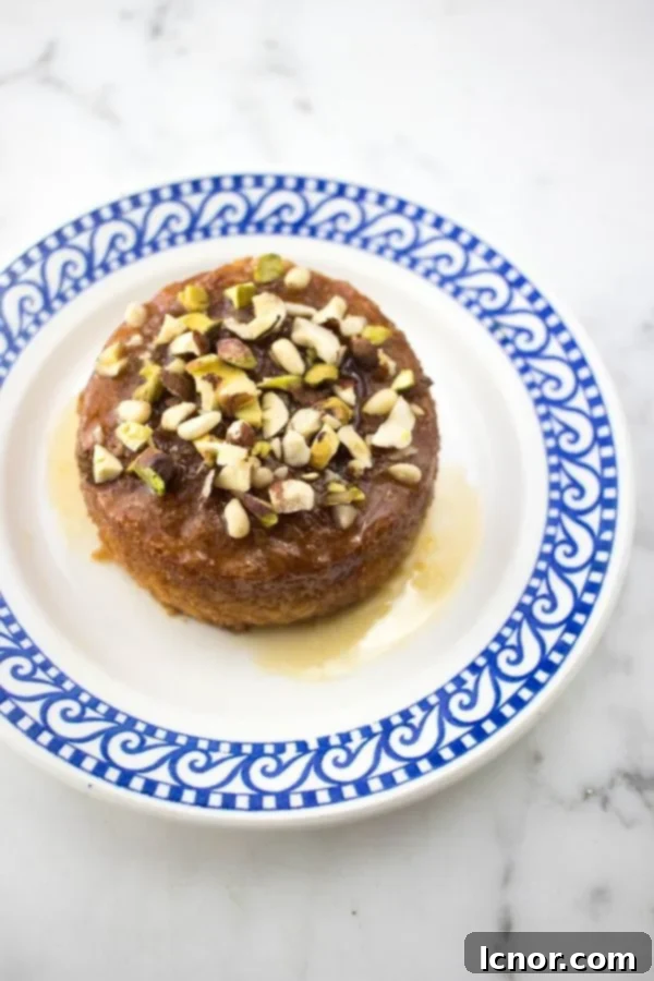 A charming small Tunisian orange cake, perfectly portioned and topped with vibrant pistachios, resting on a blue and white plate.